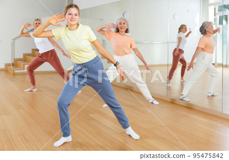 Teen girl with family doing aerobics exercises with group of people in dance center 95475842