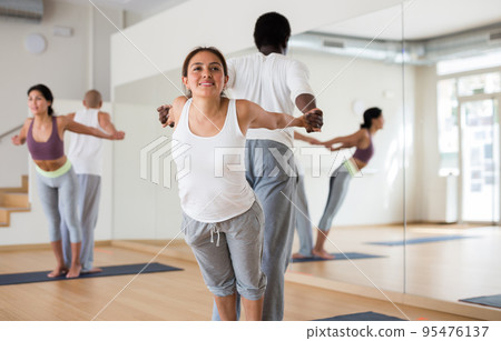 Sporty adult concentrated females and males doing stretching workout in pairs during group training Sporty adult concentrated females and males doing stretching workout in pairs during group training 95476137
