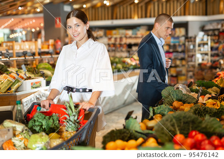 Positive young woman with shopping cart at supermarket Positive young woman with shopping cart at supermarket 95476142