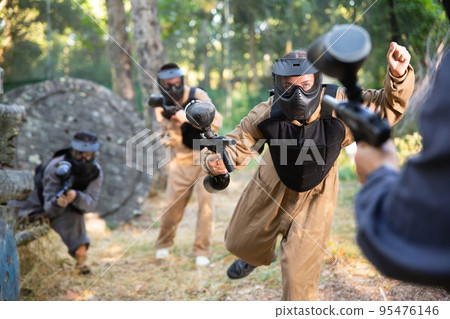 Young woman paintball player rushing through enemy lines Young woman paintball player rushing through enemy lines 95476146