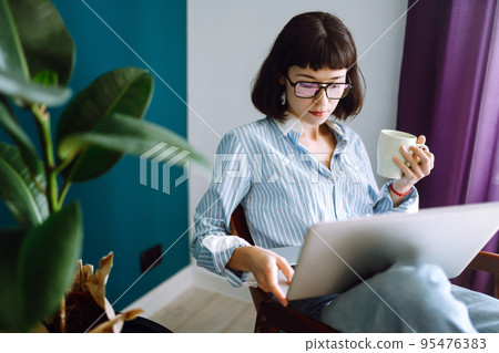Young woman freelancer sit on modern sofa and work on laptop. Education online. Working from home. 95476383