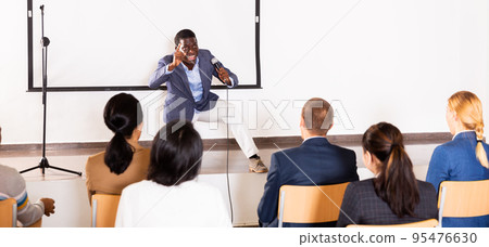 Expressive african american speaker with microphone on conference room stage Expressive african american speaker with microphone on conference room stage 95476630