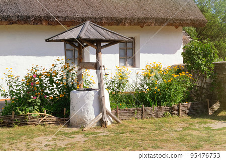 Old well near a rural hut with whitewashed walls. Village is preserving rustic traditions and culture. 95476753