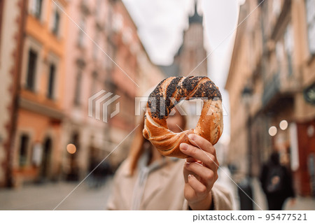 Tourists woman holding bagel obwarzanek, traditional polish cuisine prezel snack on Market square in Krakow. Tourists woman holding bagel obwarzanek, traditional polish cuisine prezel snack on Market square in Krakow. 95477521