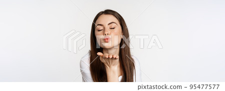 Feminine woman sending air kiss at camera, coquettish flirty pose, kissing, standing over white background 95477577