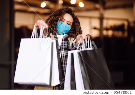 Young woman in protective medical mask with shopping bags 'near mall. Beautiful woman after shopping. Young woman in protective medical mask with shopping bags 'near mall. Beautiful woman after shopping. 95478001