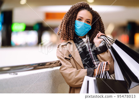 Young woman in protective medical mask with shopping bags 'near mall. Beautiful woman after shopping. 95478013