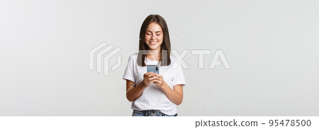 Smiling attractive girl using mobile phone and looking at screen pleased 95478500