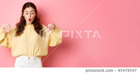 Excited cute girl checking out promo offer on bottom, pointing fingers down and saying wow, being impressed with advertisement, standing over pink background Excited cute girl checking out promo offer on bottom, pointing fingers down and saying wow, being impressed with advertisement, standing over pink background 95478547
