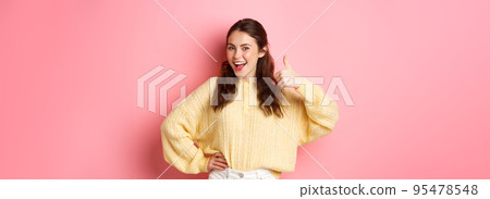 Portrait of beautiful brunette female model showing thumbs up, like your idea, give support, approve or praise something good, standing against pink background Portrait of beautiful brunette female model showing thumbs up, like your idea, give support, approve or praise something good, standing against pink background 95478548