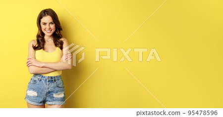 Summer holidays and people. Stylish bright girl in tank top and shorts, posing against yellow background, smiling and looking relaxed 95478596
