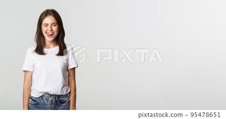 Sassy beautiful young woman winking and showing tongue flirty, white background 95478651