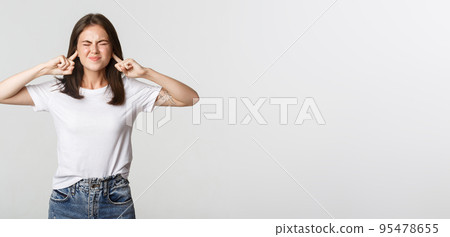 Annoyed brunette girl grimacing, shut ears with fingers from loud noise 95478655
