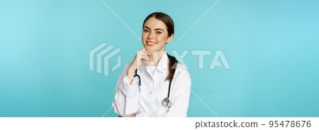 Medical staff and doctors concept. Young smiling female doctor, healthcare worker in white coat and stethoscope, looking confident, waiting patients, blue background Medical staff and doctors concept. Young smiling female doctor, healthcare worker in white coat and stethoscope, looking confident, waiting patients, blue background 95478676