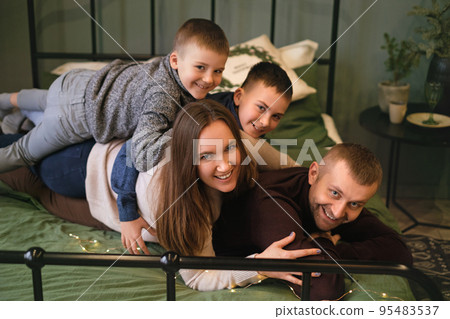 A family with their sons are having fun lying on top of each other on the bed. Happy loving family spends the weekend together A family with their sons are having fun lying on top of each other on the bed. Happy loving family spends the weekend together 95483537