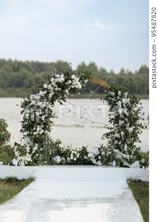 Elegant wedding arch with fresh flowers, vases on background of river and blue sky. Elegant wedding arch with fresh flowers, vases on background of river and blue sky. 95487820