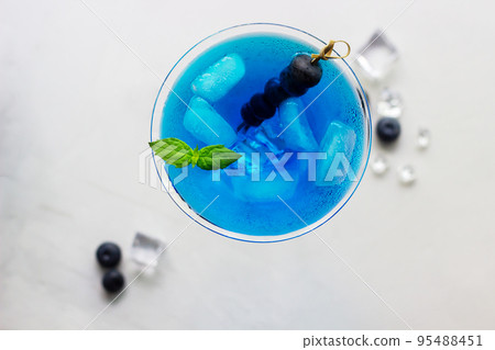 Top view of blue cocktail in martini glass with ice cubes, mint and bluberries 95488451