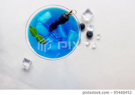 Top view of blue cocktail in martini glass with ice cubes, mint and bluberries 95488452