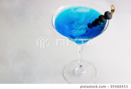 Close-up of blue cocktail in martini glass with ice cubes and bluberries 95488453