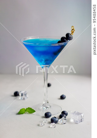 Blue cocktail in martini glass with ice cubes, mint and bluberries 95488458