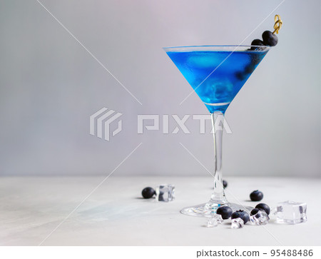 Blue cocktail in martini glass with ice cubes and bluberries 95488486