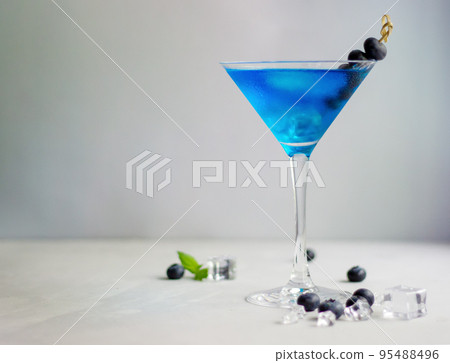 Blue cocktail in martini glass with ice cubes, mint and bluberries 95488496