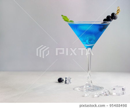 Blue cocktail in martini glass with ice cubes, mint and bluberries 95488498
