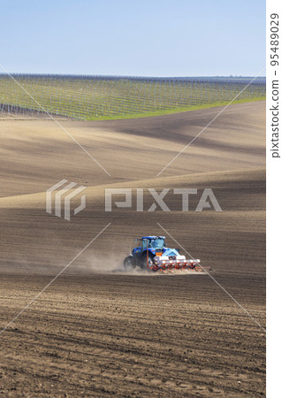 Tractor with seed drill in early spring landscape 95489029
