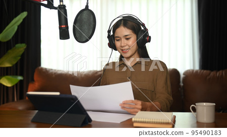 Pretty young woman wearing headphone and talking through microphone recording podcast in small home studio Pretty young woman wearing headphone and talking through microphone recording podcast in small home studio 95490183
