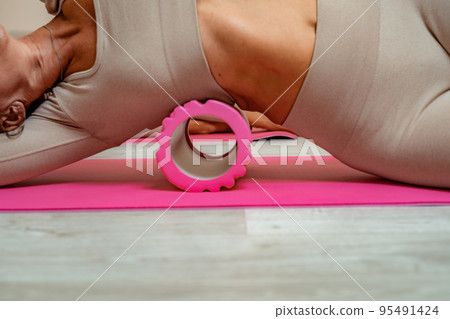 Fit athletic women in beige sportswear ride on a pink foam myofascial massage roller, massaging their muscles on the floor of a yoga mat in the gym. Active girls do a fitness workout in the gym. MFR Fit athletic women in beige sportswear ride on a pink foam myofascial massage roller, massaging their muscles on the floor of a yoga mat in the gym. Active girls do a fitness workout in the gym. MFR 95491424