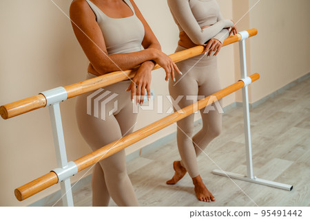 Near the barre, in the choreographic hall, two women in a beige top and leggings are engaged. Near the barre, in the choreographic hall, two women in a beige top and leggings are engaged. 95491442