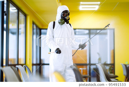 Man wearing protective suit disinfecting assembly hall with spray. Disinfecting of office. COVID-19. Man wearing protective suit disinfecting assembly hall with spray. Disinfecting of office. COVID-19. 95491533
