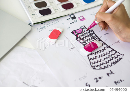 Closeup fashion designer hand use magic pen painting on pattern for cloth. Brightly colored fabric samples are on the workbench. 95494000