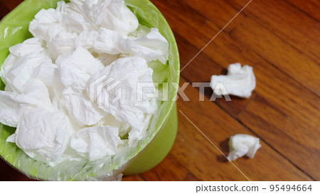 A small garbage bin full with used tissue paper, on a wooden floor. 95494664