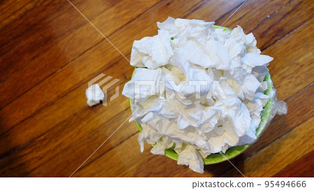 Top view of a small garbage bin full with used tissue paper, on wooden floor. 95494666
