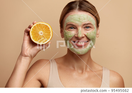 Laughing Face Mask Woman Hold Orange. Positive Woman with Clay Face Mask Laughing Face Mask Woman Hold Orange. Positive Woman with Clay Face Mask 95495082