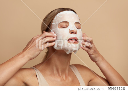 Beauty Woman Applying Face Mask. Portrait Of Girl Applying White Sheet Mask Beauty Woman Applying Face Mask. Portrait Of Girl Applying White Sheet Mask 95495128