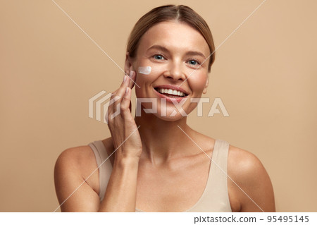 Skin Care Woman Applying Cream on Cheek. Beautiful Smiling Girl Putting Cream 95495145