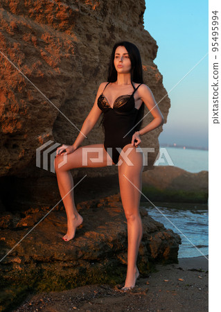 Sexy girl in a black swimsuit in the sea against stones 95495994