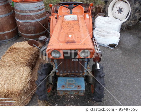 A small orange tractor parked in a field, facing forward. A small orange tractor parked in a field, facing forward. 95497556