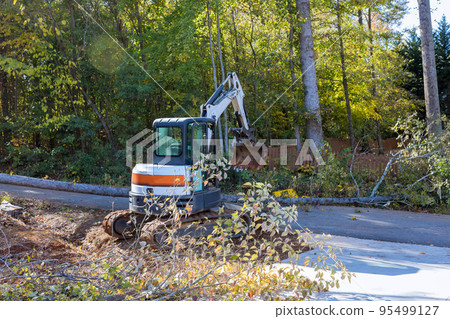 Fallen tree after storm damaged fence after hurricane an uprooted trees fell in street with tractor cleanup raise fallen trees Fallen tree after storm damaged fence after hurricane an uprooted trees fell in street with tractor cleanup raise fallen trees 95499127
