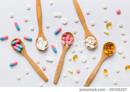 Vitamin capsules in a spoon on a colored background. Pills served as a healthy meal. Red soft gel vitamin supplement capsules on spoon 95500297