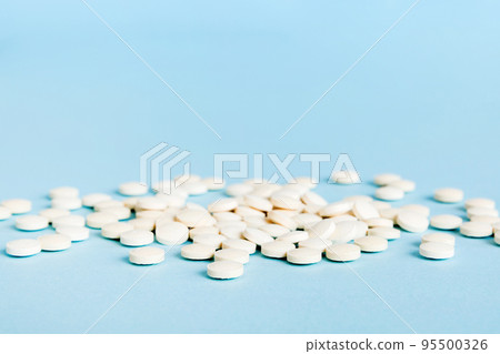 Heap of white pills on colored background. Tablets scattered on a table. Pile of red soft gelatin capsule. Vitamins and dietary supplements concept 95500326
