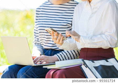 A young female college student who touches a smartphone and a personal computer on an outdoor bench 95501714