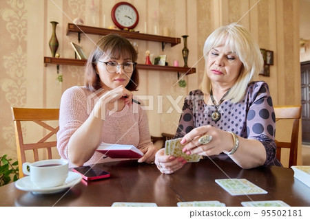 Two middle aged women laying out cards at home on the table 95502181