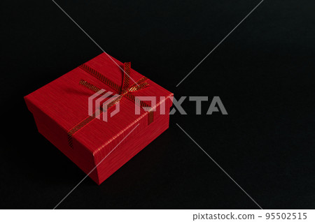 Still life red cardboard present box with a tied bow isolated on a black background with advertising copy space. Web banner. Top view of Christmas gift with surprise, packed in an elegant gift box. Still life red cardboard present box with a tied bow isolated on a black background with advertising copy space. Web banner. Top view of Christmas gift with surprise, packed in an elegant gift box. 95502515