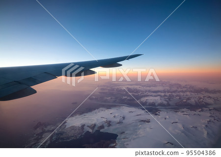 Commercial Aviation Jetplane flying over the ice mountain landscape on the Ocean Coast of Greenland. 95504386