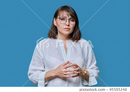 Serious confident middle aged woman on blue background Serious confident middle aged woman on blue background 95505248