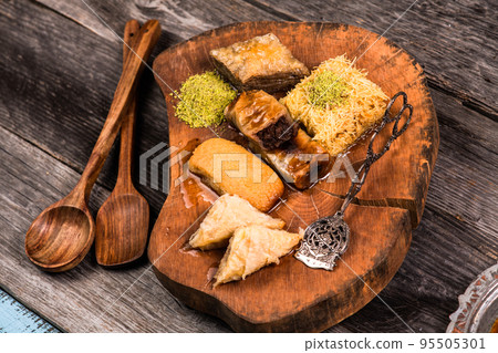 Ramadan Kareem, traditional Turkish middle eastern Iftar sweets Baklava with pistachios and fresh honey on rustic wooden plate and vintage blue background table. Top view. Ramadan Kareem, traditional Turkish middle eastern Iftar sweets Baklava with pistachios and fresh honey on rustic wooden plate and vintage blue background table. Top view. 95505301
