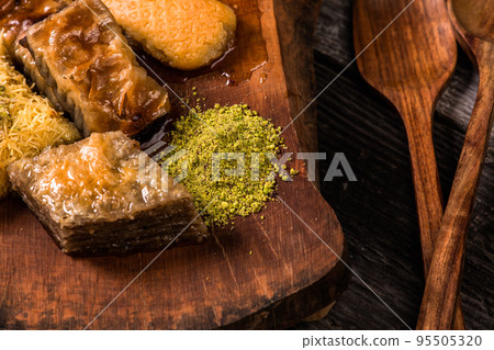 Ramadan Kareem, traditional Turkish middle eastern Iftar sweets Baklava with pistachios and fresh honey on rustic wooden plate and vintage blue background table. Top view. Ramadan Kareem, traditional Turkish middle eastern Iftar sweets Baklava with pistachios and fresh honey on rustic wooden plate and vintage blue background table. Top view. 95505320